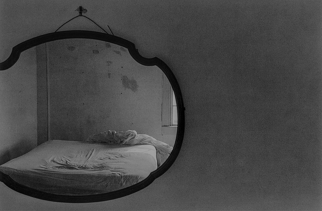 Schwarz-weiß Fotografie eines Spiegels in dem ein Bett zusehen ist