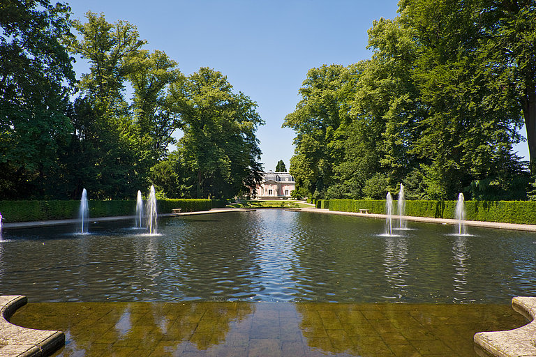 Water pool with water fountains in the French Garden overlooking the pink Corps de Logis.
