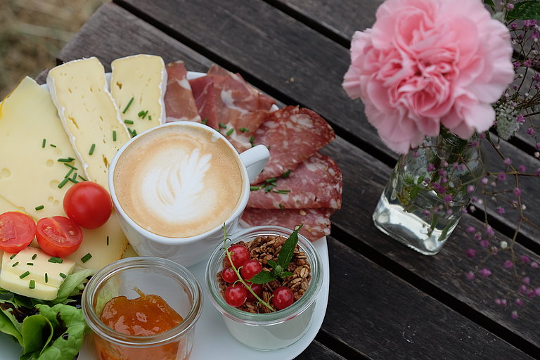 Various cold cuts and a coffee on a plate next to a flower