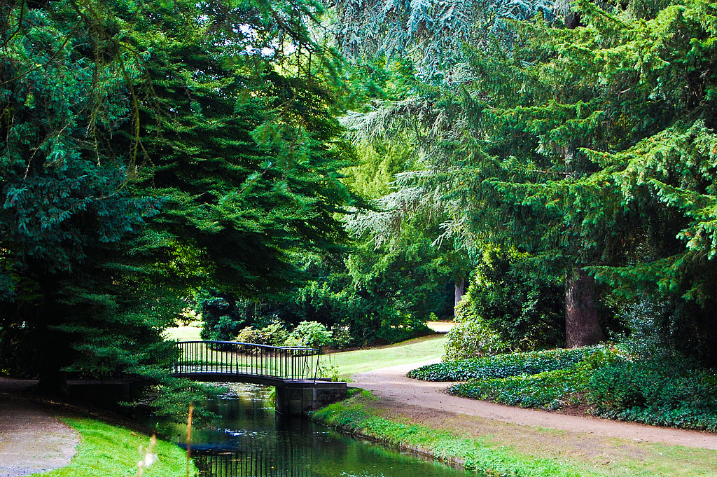 Wasserkanal, mittig eine Brücke, umringt von Bäumen, Grasfläche und Gehwegen