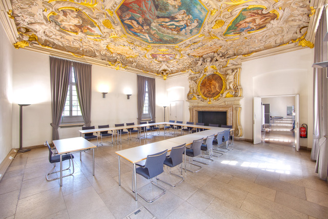 U-shaped table grouping in a room with a large painting under the ceiling